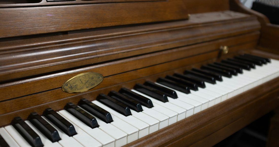A walnut upright piano with the key lid open, ready for tuning
